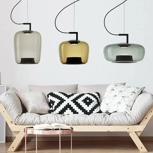 Danish glass pendant light trio in soft green, yellow, and gray hanging above a modern sofa with patterned cushions.