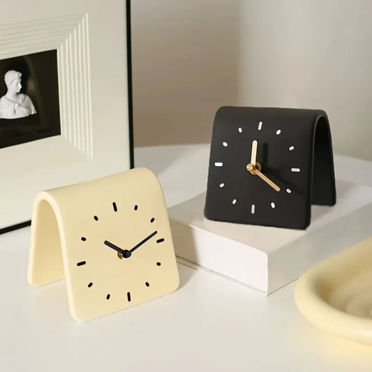 Two minimalistic table clocks, one beige and one black, on a light surface.