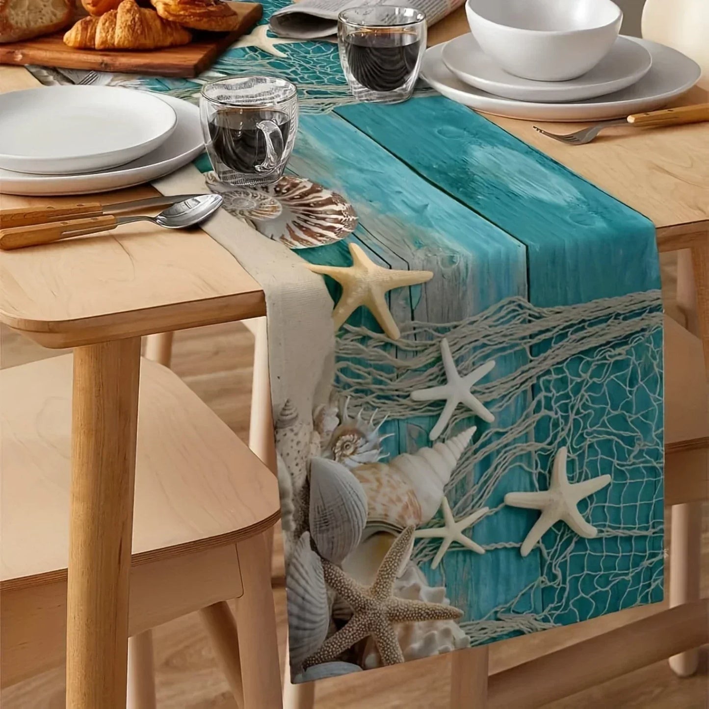 Table setting with a decorative table runner featuring starfish and shells on a wooden table.