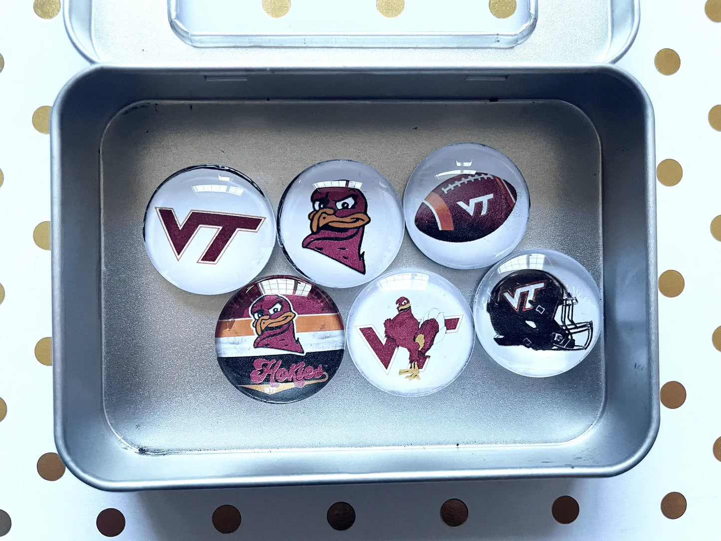 Set of Virginia Tech-themed pins in a metal case on a polka dot background