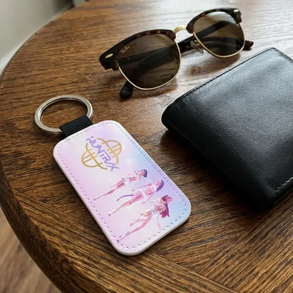 Keychain with logo and character design on a wooden surface with sunglasses and wallet.