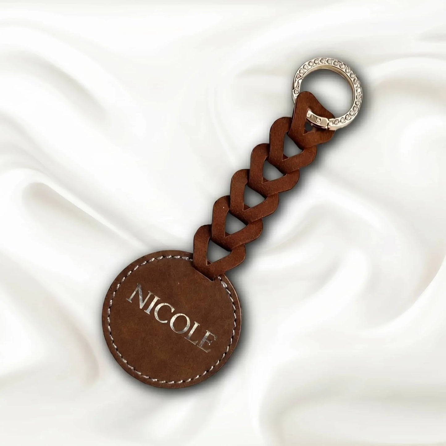 Brown leather keychain with braided design and 'NICOLE' engraving on a white fabric background