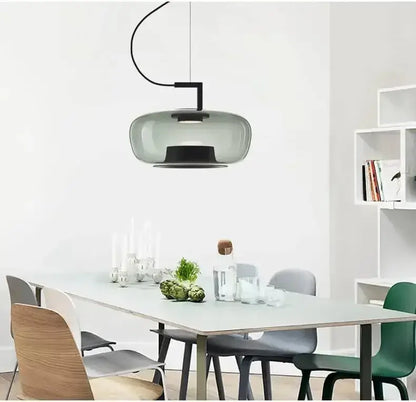 Danish glass pendant light hanging above a modern dining table with stylish chairs and decorative elements.