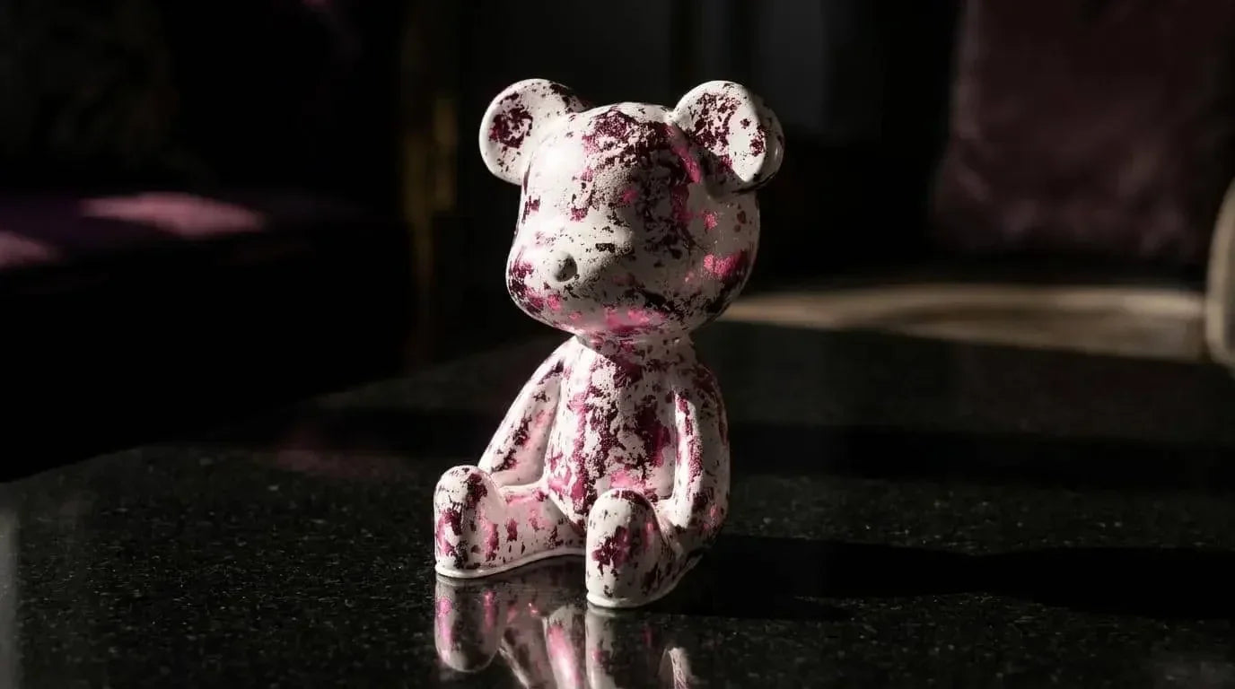 Small teddy bear figurine with pink speckles on a dark surface