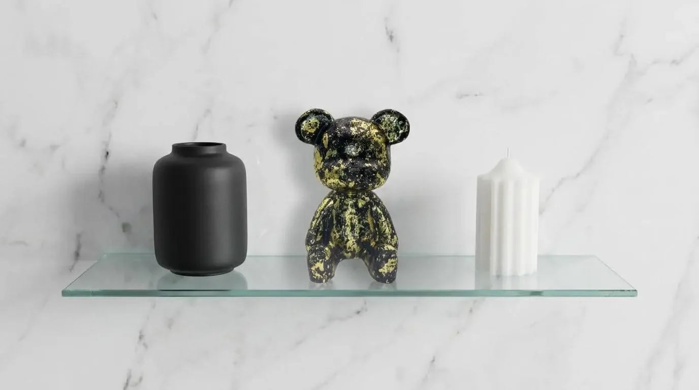 Decorative bear figurine and black vase on a glass shelf against a marble wall.
