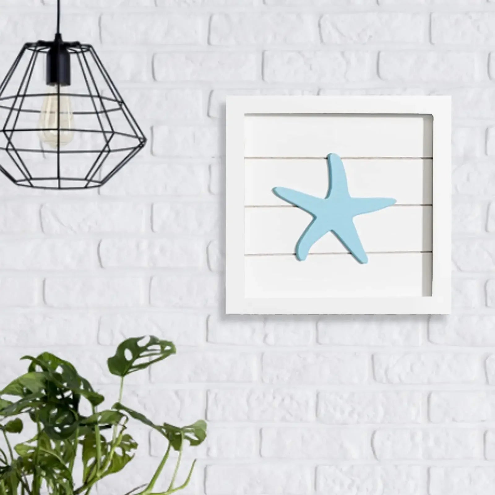 Framed artwork of a blue starfish on a white brick wall with a black geometric pendant light.