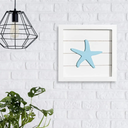 Framed artwork of a blue starfish on a white brick wall with a black geometric pendant light.