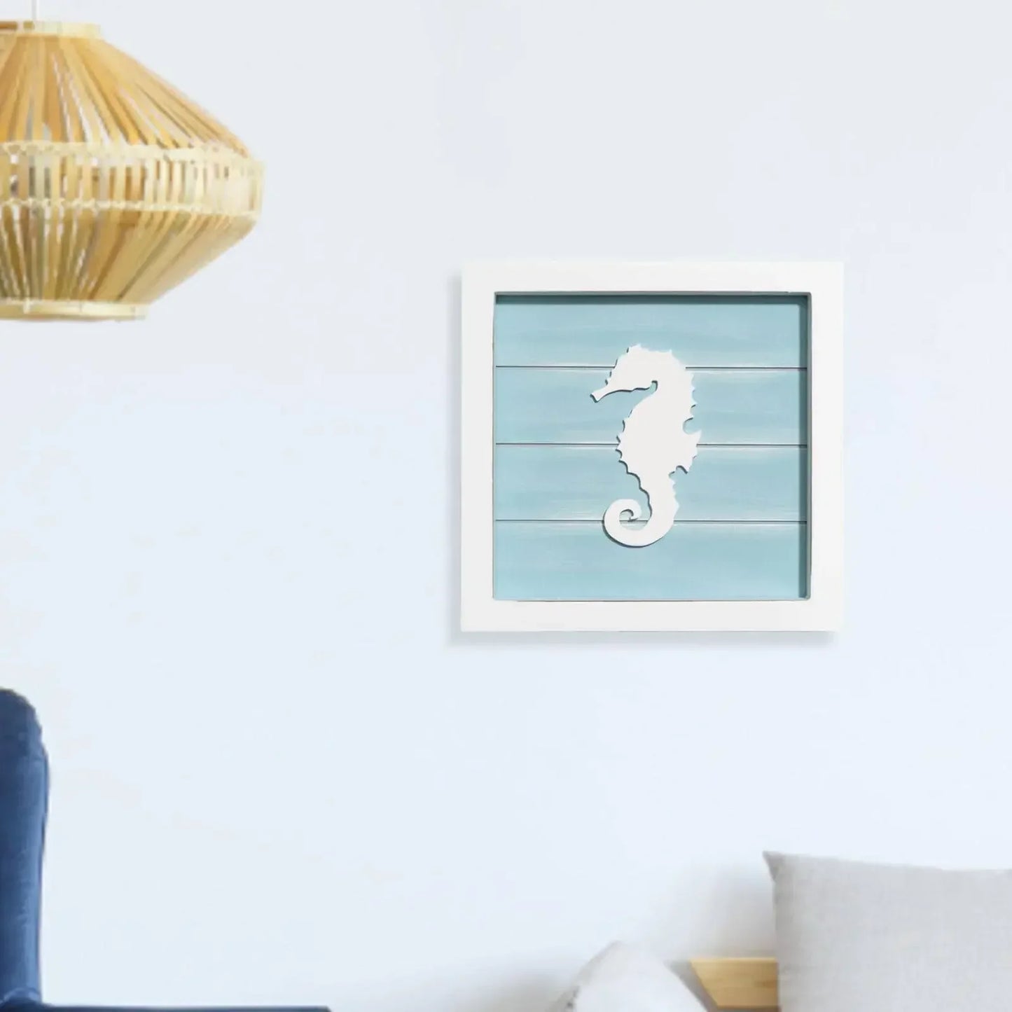 Framed artwork of a seahorse on a light blue background in a room with a lamp and chair.