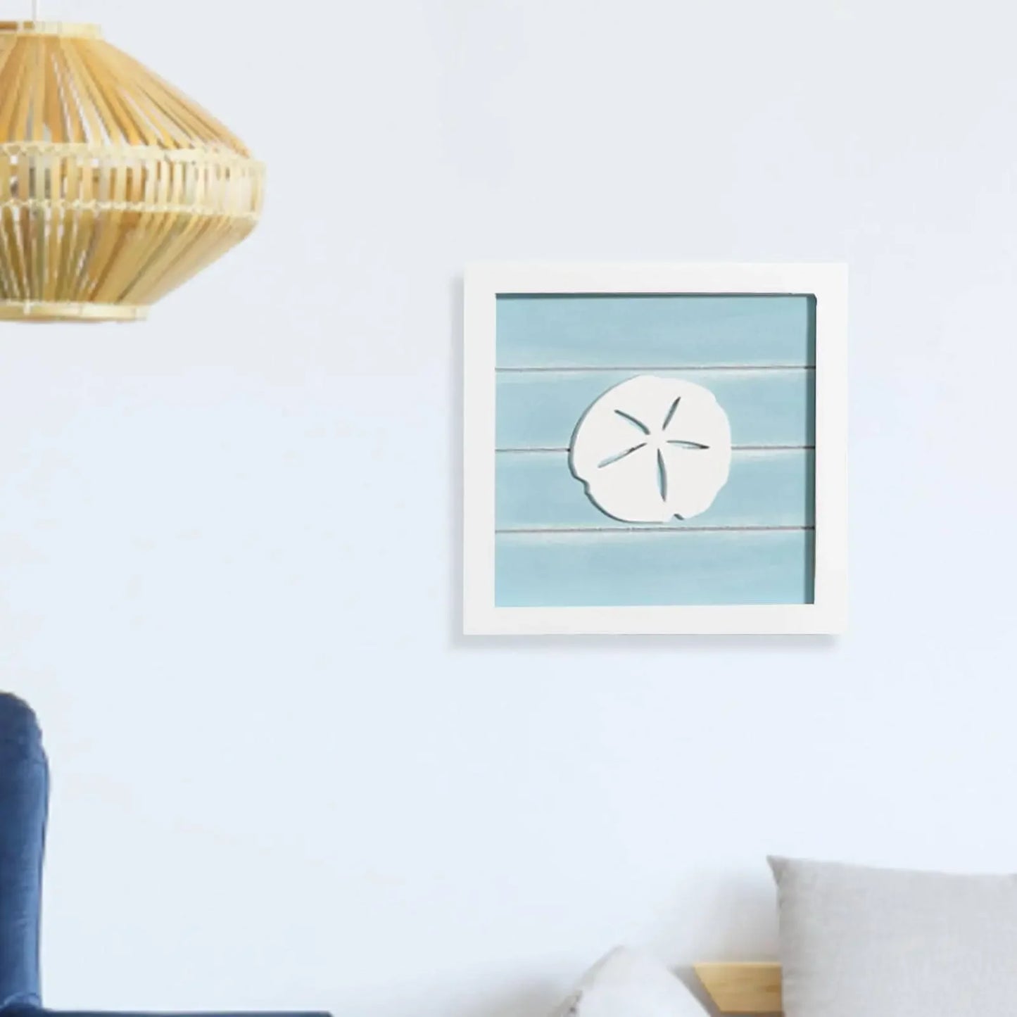 Framed artwork with a sand dollar design on a blue striped background, hanging on a white wall.