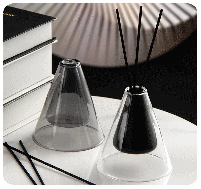 Triangle Glass Aromatherapy Vase with black sticks on a white surface.