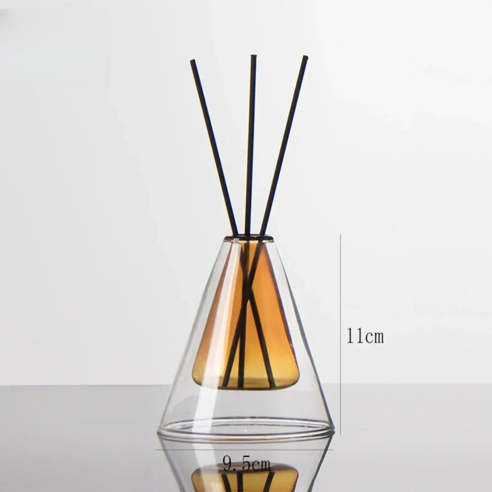 A clear glass diffuser with amber-colored base and black sticks on a white background.