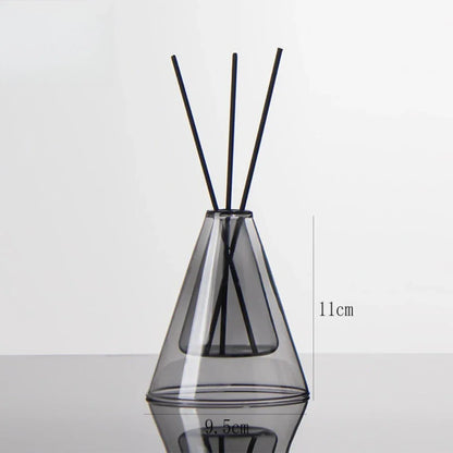 Clear glass diffuser vase with black sticks on a white background