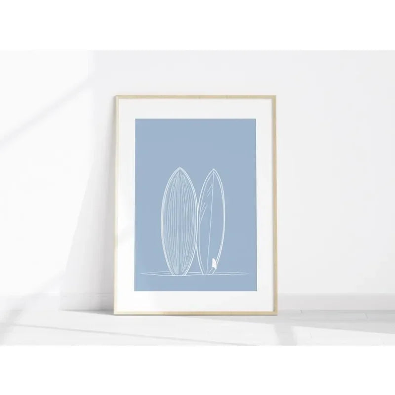 Framed artwork with two surfboards on a light blue background, displayed on a white surface.